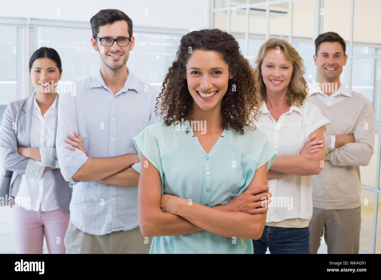 Casual business team smiling at camera with arms crossed in the office ...