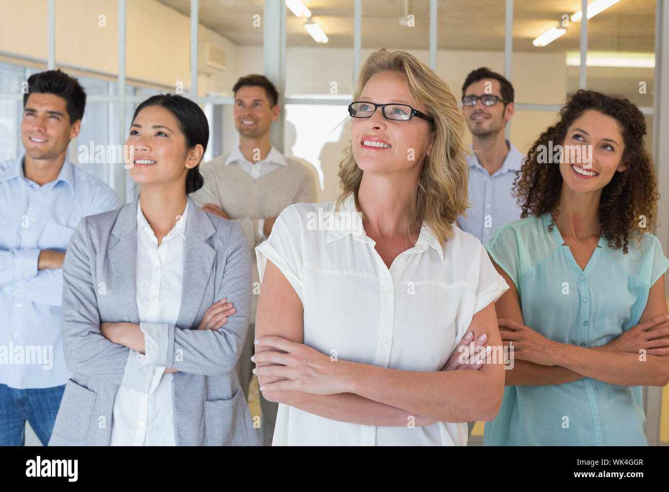 Casual business team smiling with arms crossed looking up in the office ...