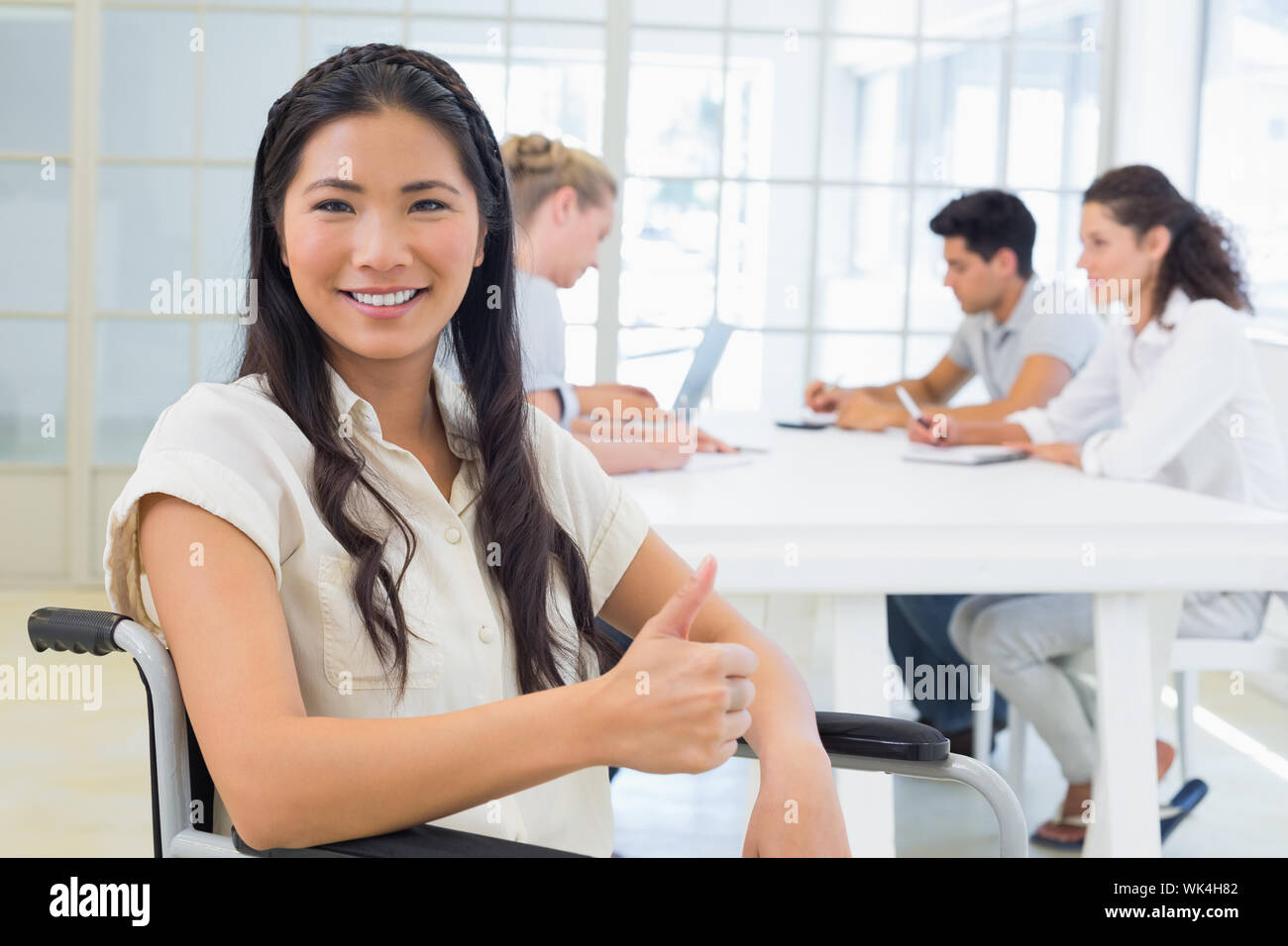 Casual businesswoman in wheelchair smiling at camera giving thumbs up ...