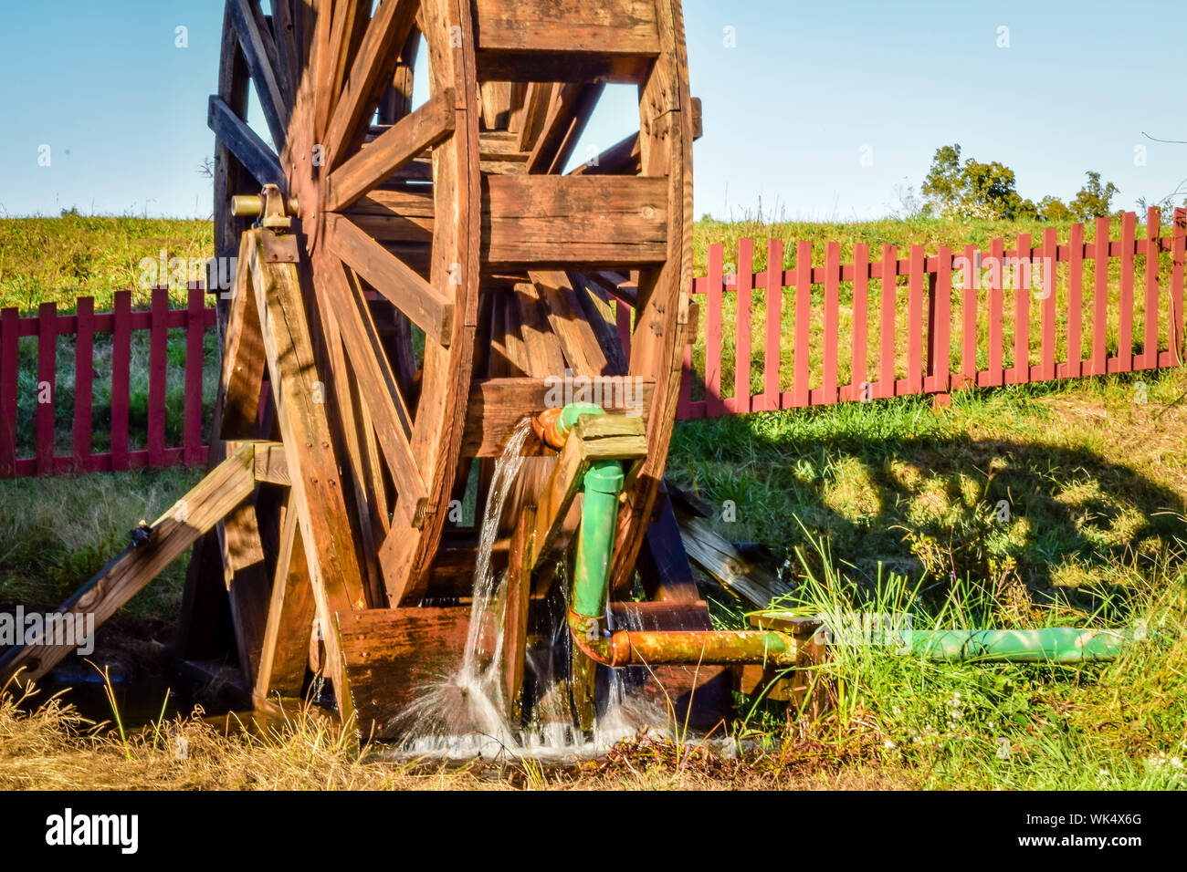 Wooden Water Wheel On Grassy Field By Fence Against Sky Stock