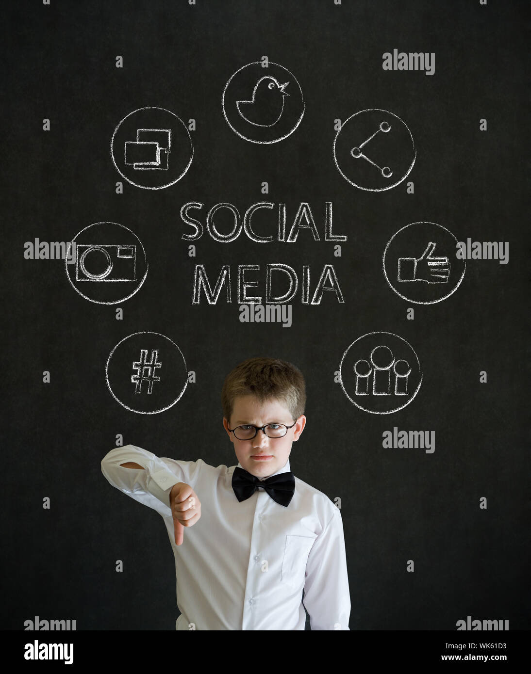 Thumbs down boy dressed up as business man with social media icons on blackboard background Stock Photo