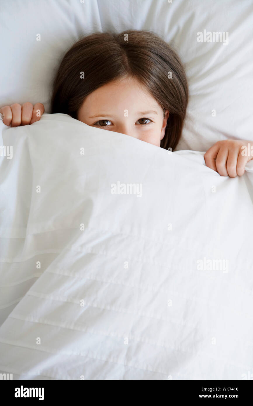 High angle portrait of little girl in bed pulling blanket over face