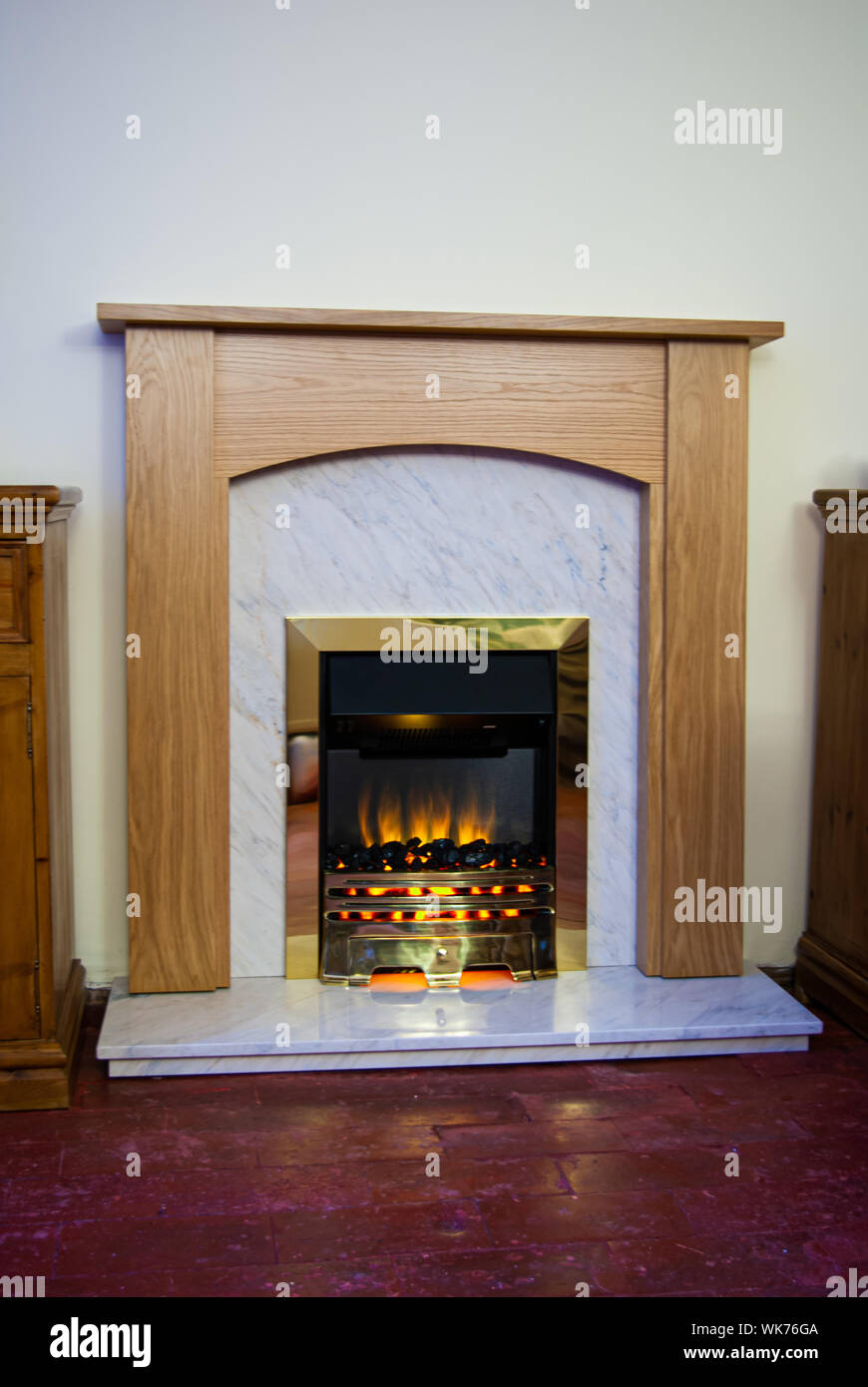 New modern wooden beech fireplace with marble inset and a coal-effect electric fire on red quarry-tiles floor Stock Photo