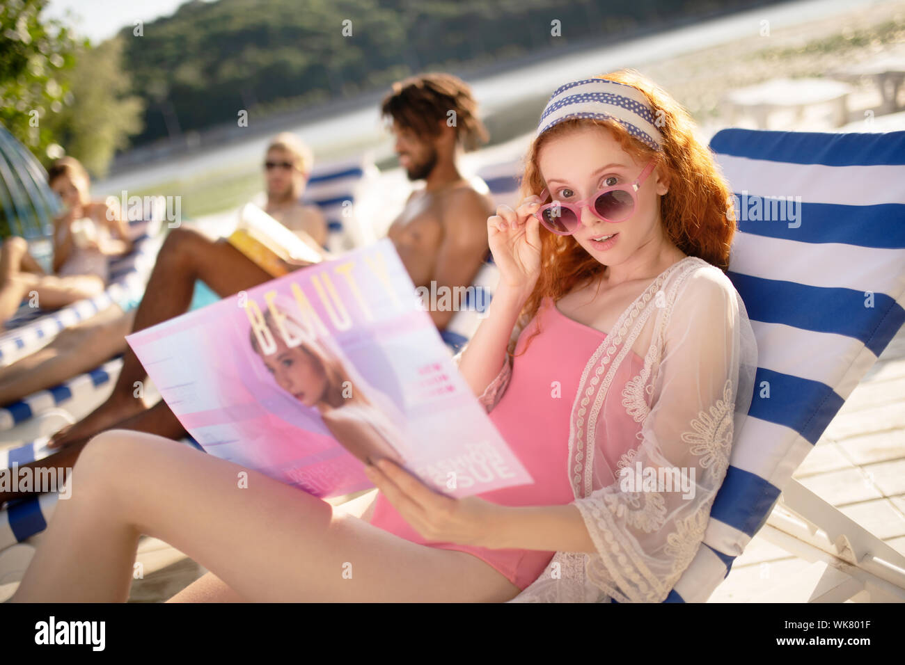 Woman wearing pink sunglasses reading beauty magazine Stock Photo