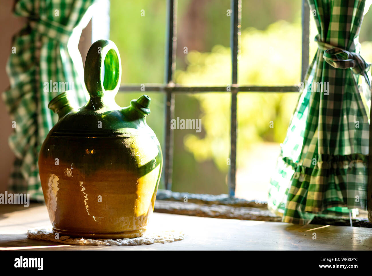 painted green bowl for drinking water on a wooden table, with a lattice window and green curtains, sunset light enters through the window Stock Photo