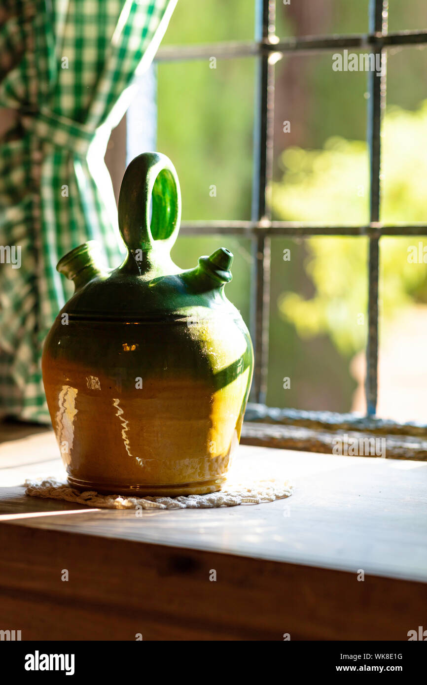 painted green bowl for drinking water on a wooden table, with a lattice window and green curtains, sunset light enters through the window Stock Photo