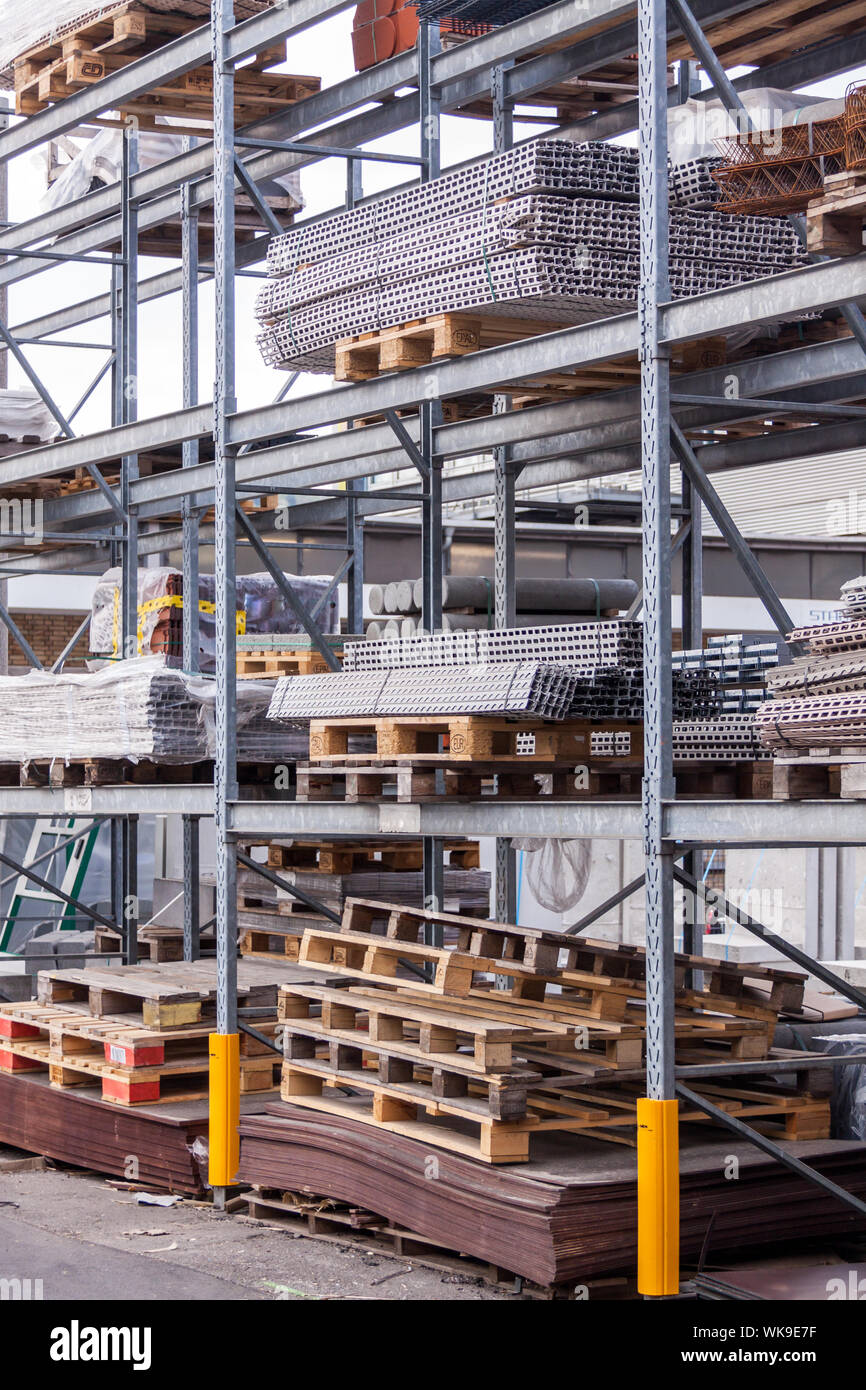 Building and construction materials for sale stored on metal shelves outdoors in a warehouse yard together with wooden pallets for loading, distributi Stock Photo