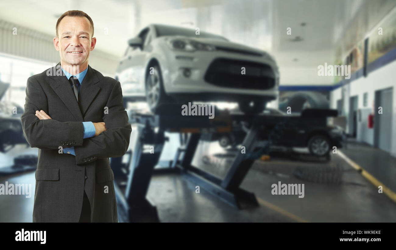 Car salesman stands with arms crossed next to a car on a lift in the dealership Stock Photo