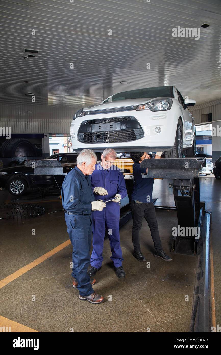 Mechanic team in the workshop at the main inspection with car on the lift Stock Photo