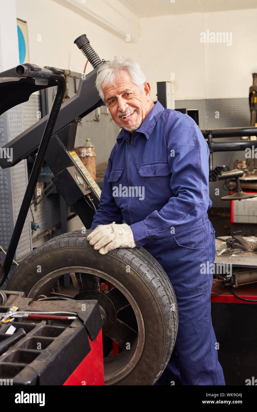 Senior as a car mechanic with experience in hoisting tires at the auto