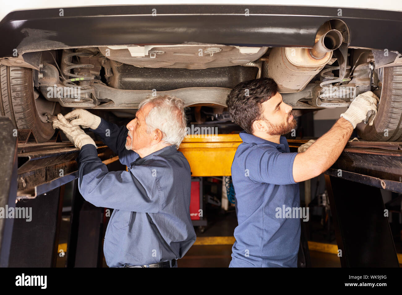 Two car mechanics inspect the car's suspension and shock absorbers