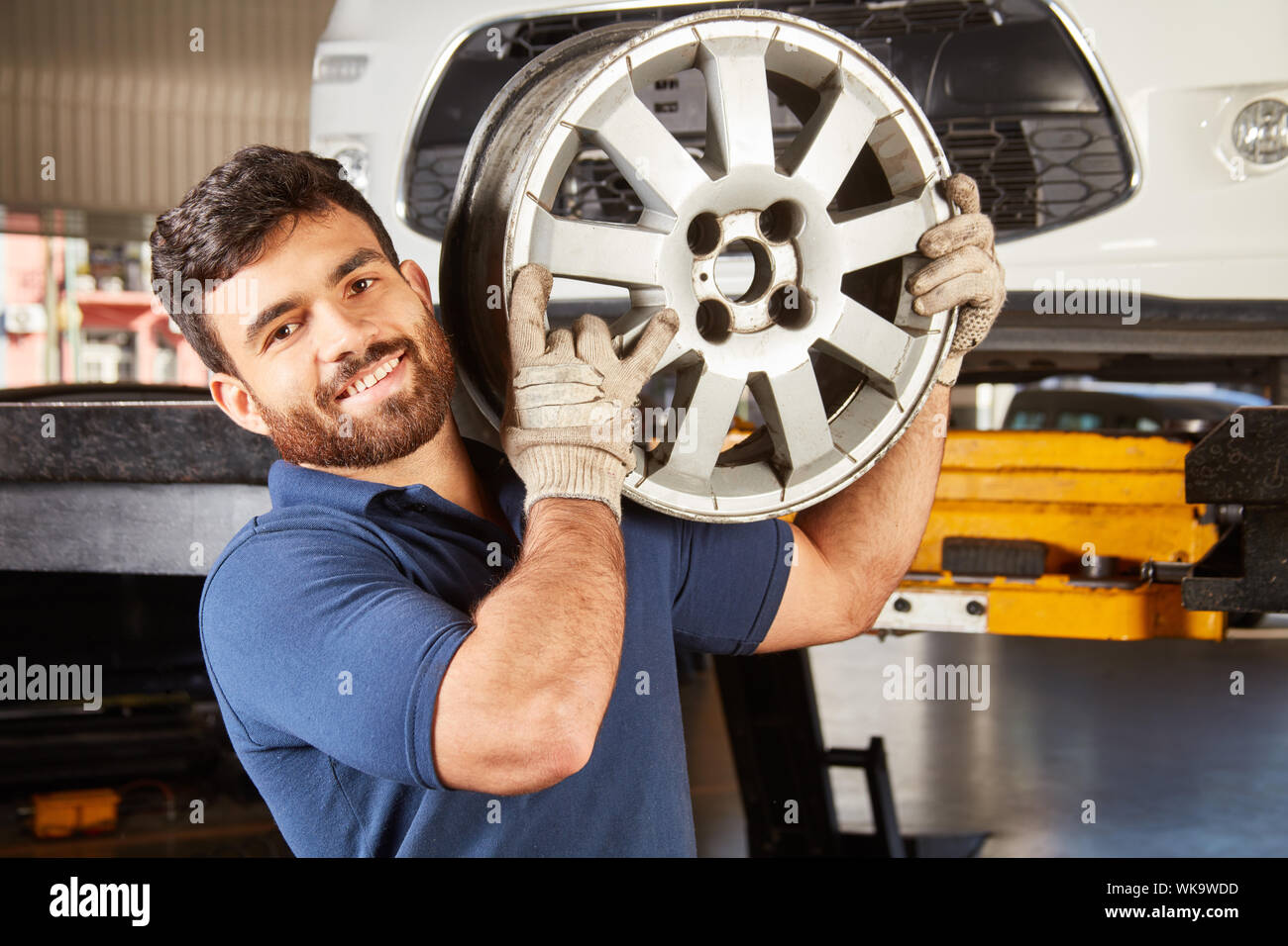 Young man as mechanic apprentice with car rim while changing wheels in