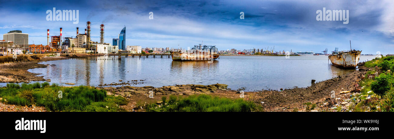 Uruguay, port of Montevideo. Wrecks of boats that have run aground in the natural harbour. On the left, the red and white chimneys of the thermal powe Stock Photo