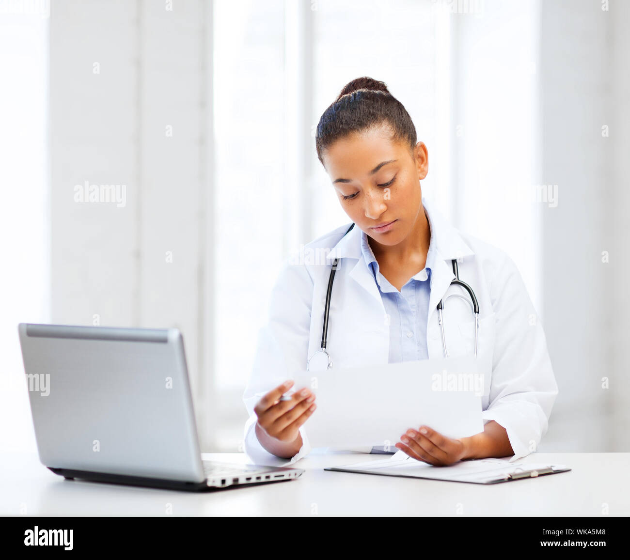 healthcare, medical and technology concept - african female doctor with laptop pc writing prescription Stock Photo