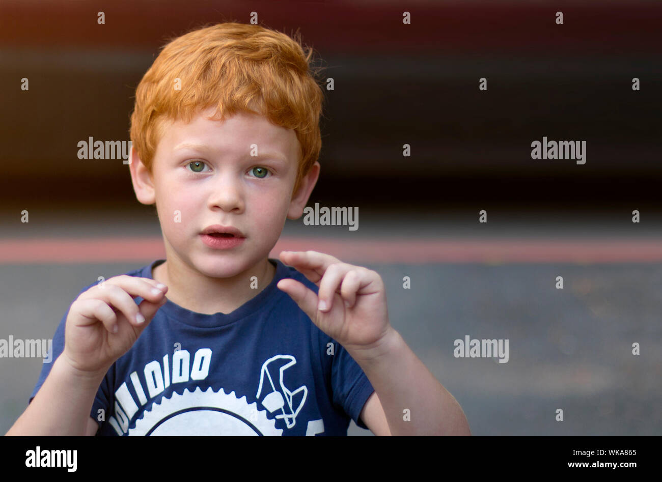 Portrait European boy with green eyes. Child with curly ginger hair. Talking with sign language. Boy talking nonverbal. Hearing loss. Deaf disability Stock Photo