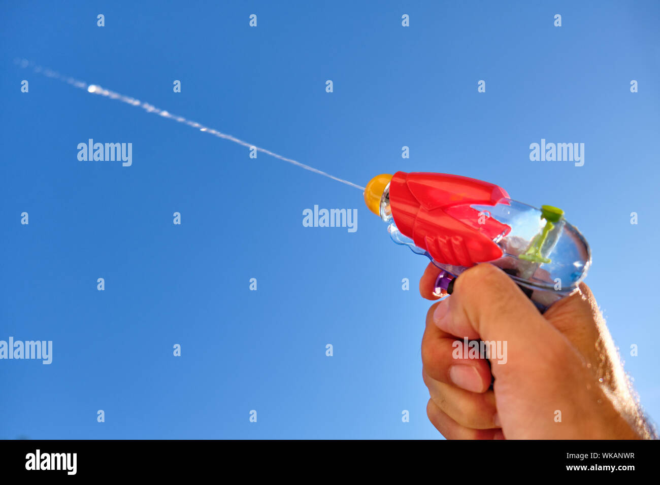 Colorful water pistol spraying out a jet of water in a caucasian male hand in front of  the blue sky of a sunny summer day Stock Photo
