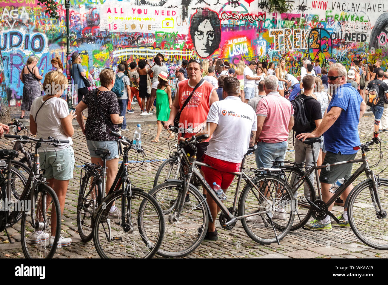 Crowds of people Prague tourists and a group of people city bikers stopped in front of the John Lennon Wall Prague tour Czech Republic Stock Photo