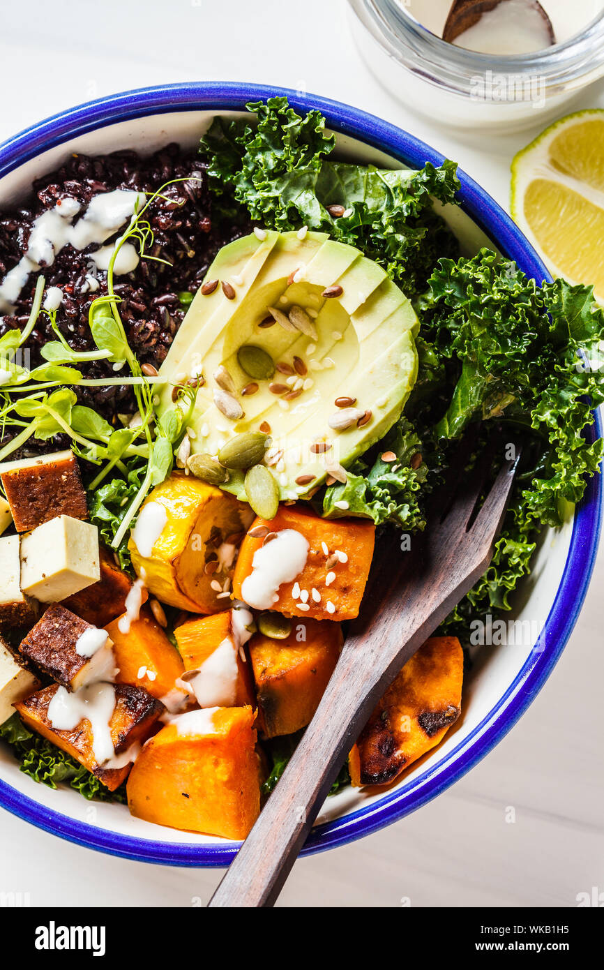 Buddha bowl salad with black rice, avocado, tofu, yam, kale and tahini dressing, white