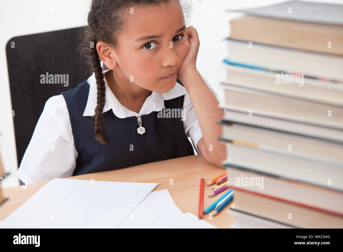 Bullying concept sad mixed race biracial African American schoolgirl or girl sitting at school desk with books, pencils and papers looking scared or d Stock Photo