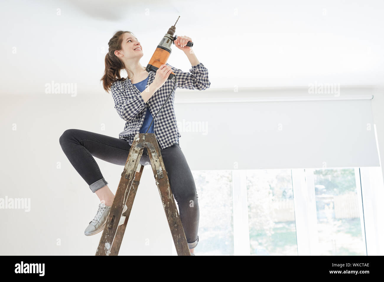 Young woman as a handyman with drill at the hole drill on the ceiling in the new house Stock Photo