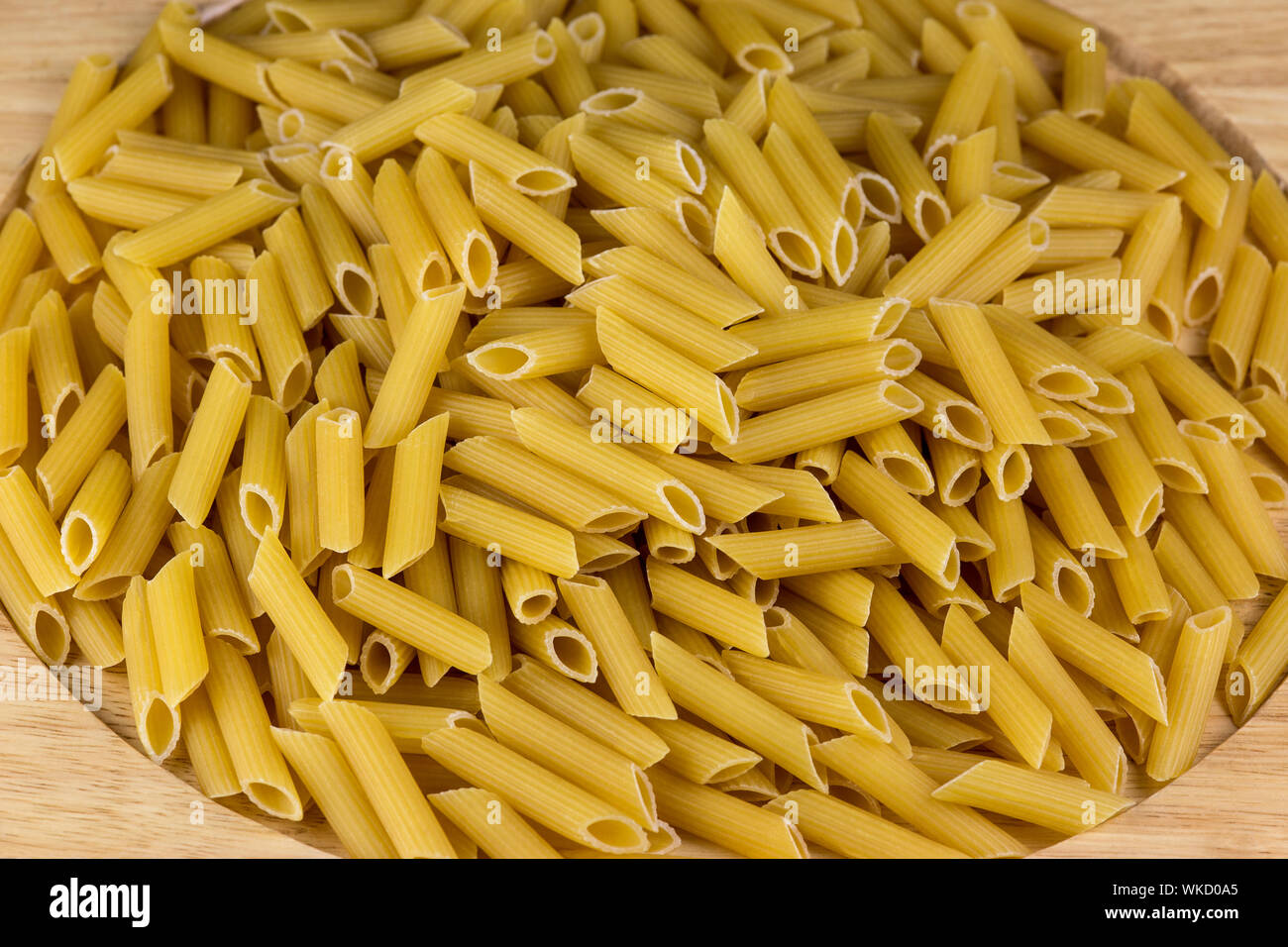 Uncooked penne pasta tubes on a wooden platter Stock Photo