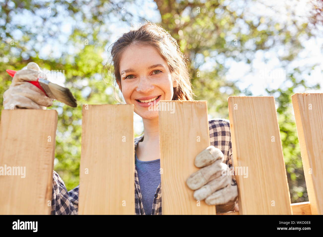 Smiling young woman in fence stroke with wood color in summer in the garden Stock Photo