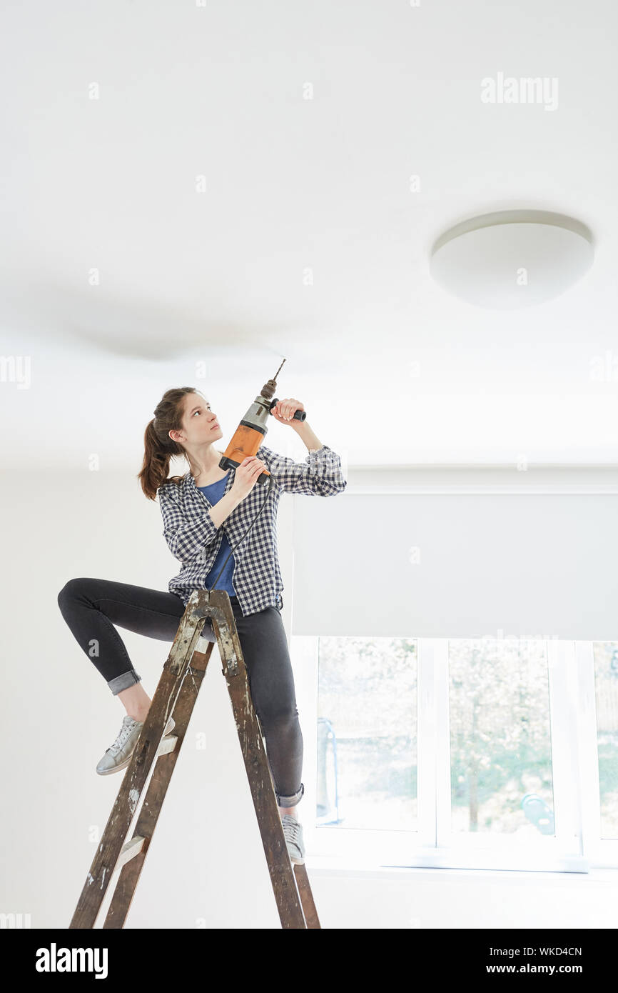 Woman as a handyman on a ladder with a drill at the hole drilling at the ceiling Stock Photo