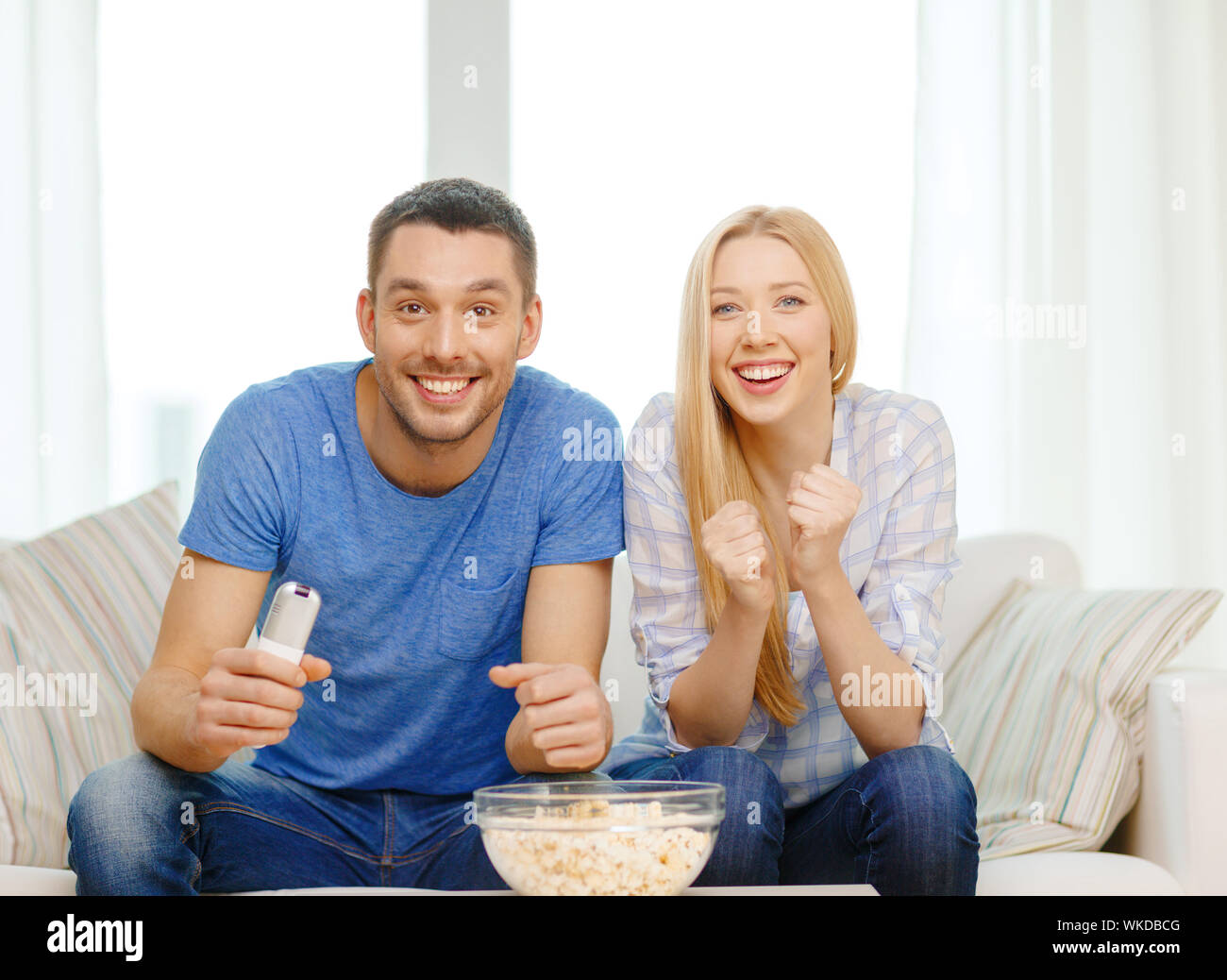 food, love, family, sports, entretainment and happiness concept - smiling couple with popcorn cheering sports team at home Stock Photo