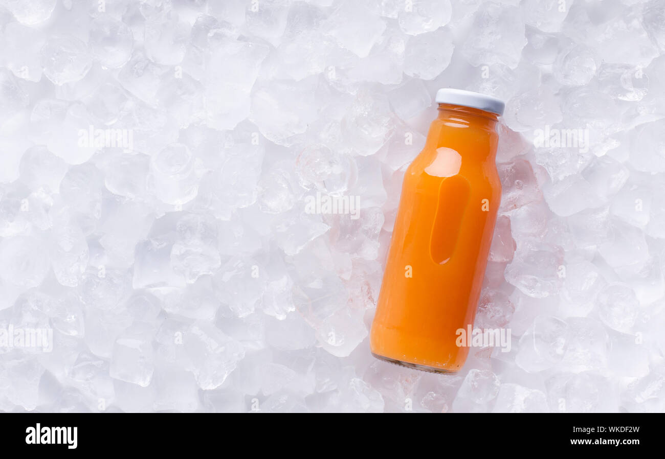 Orange detox juice in glass bottle on ice cubes background Stock Photo