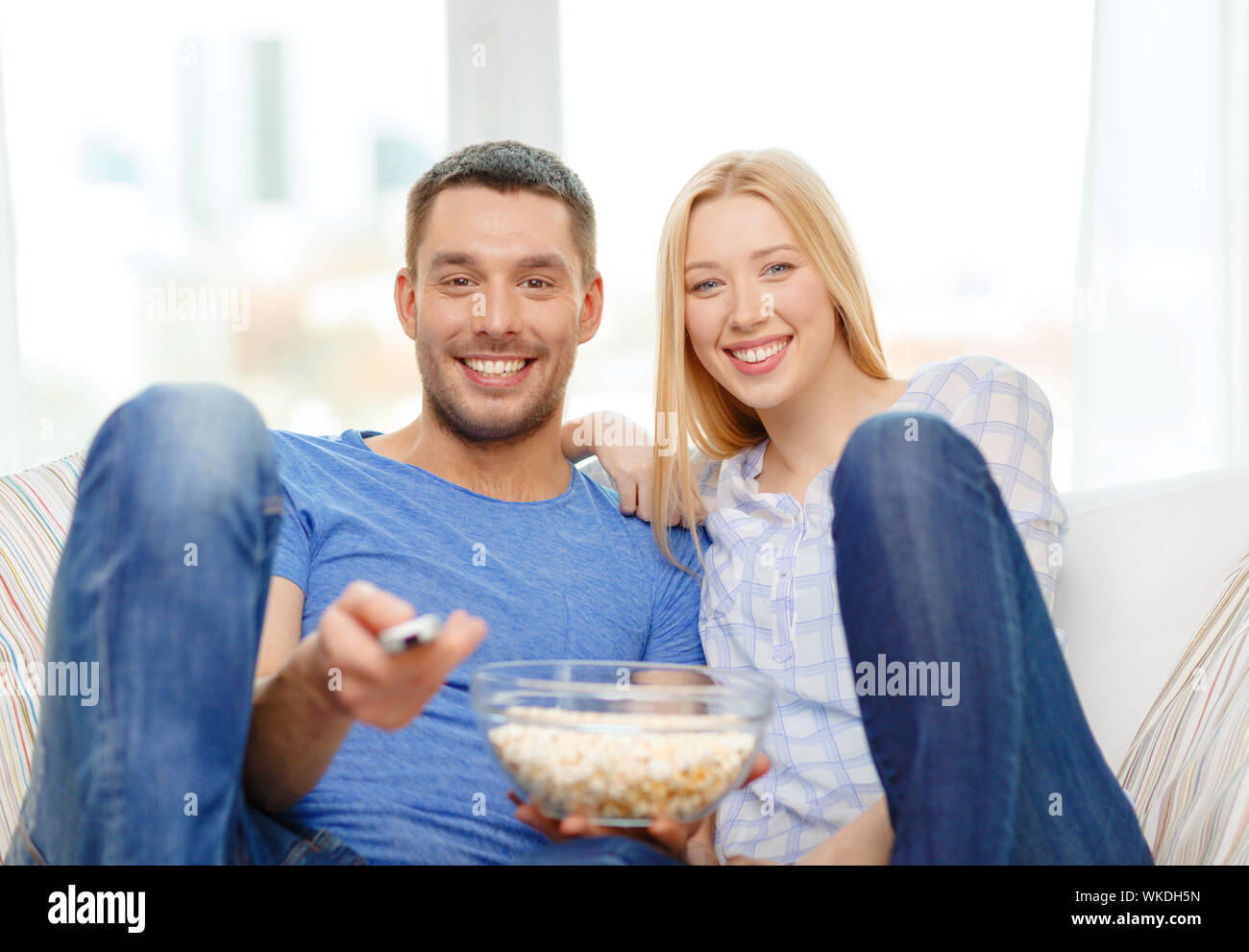 food, love, family and happiness concept - smiling couple with popcorn watching movie at home Stock Photo