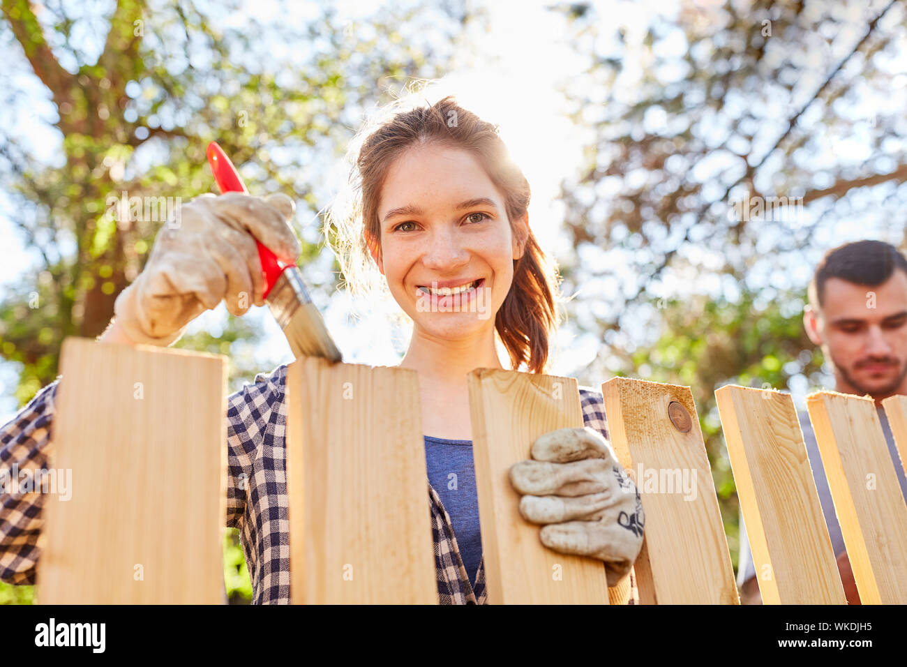 Young woman in garden with brush at fence paint with wood paint as home improvement Stock Photo