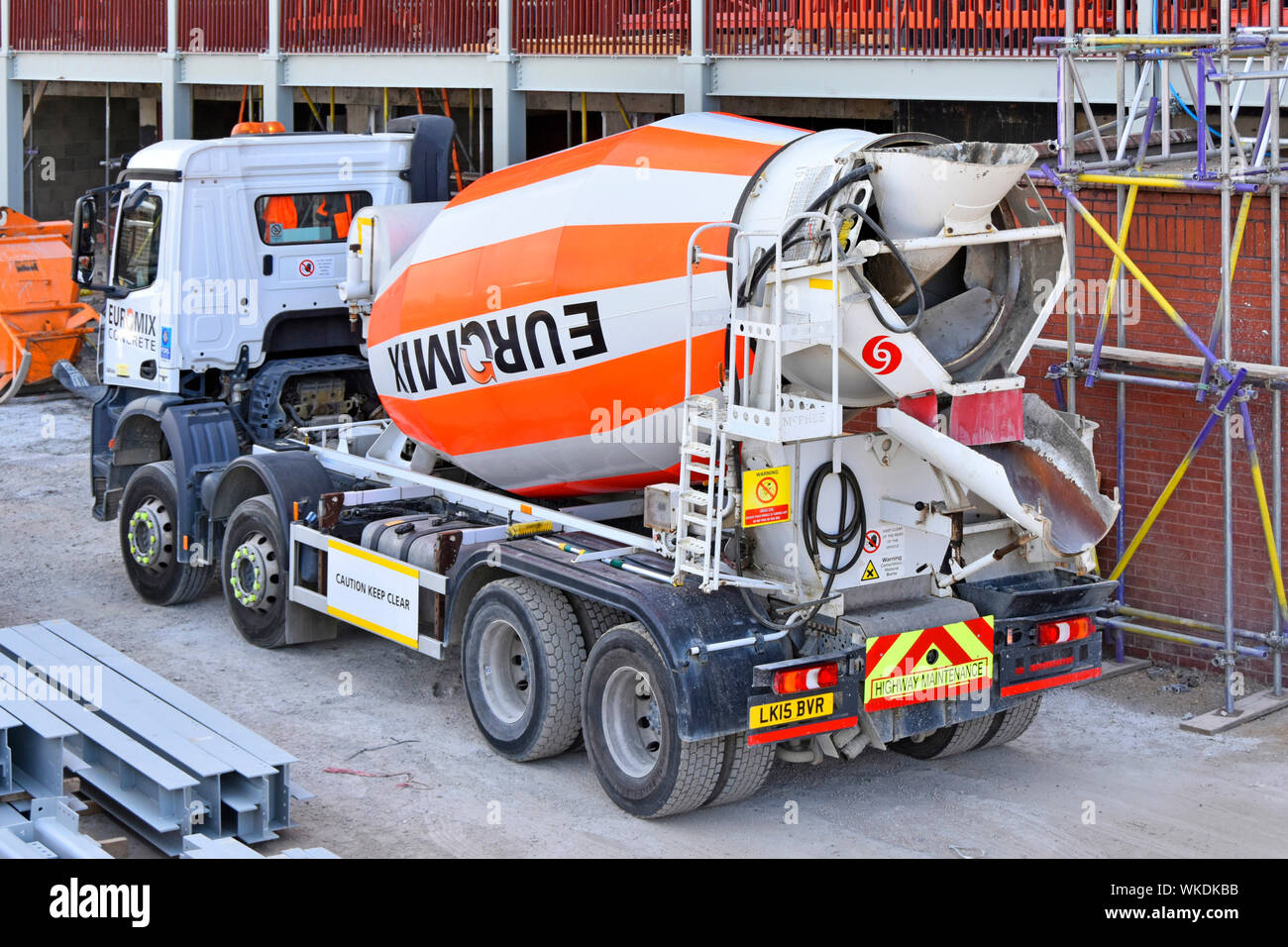 London construction building site Euromix delivery mixer lorry truck loaded with ready mix cement concrete reversing beside scaffolding England UK Stock Photo