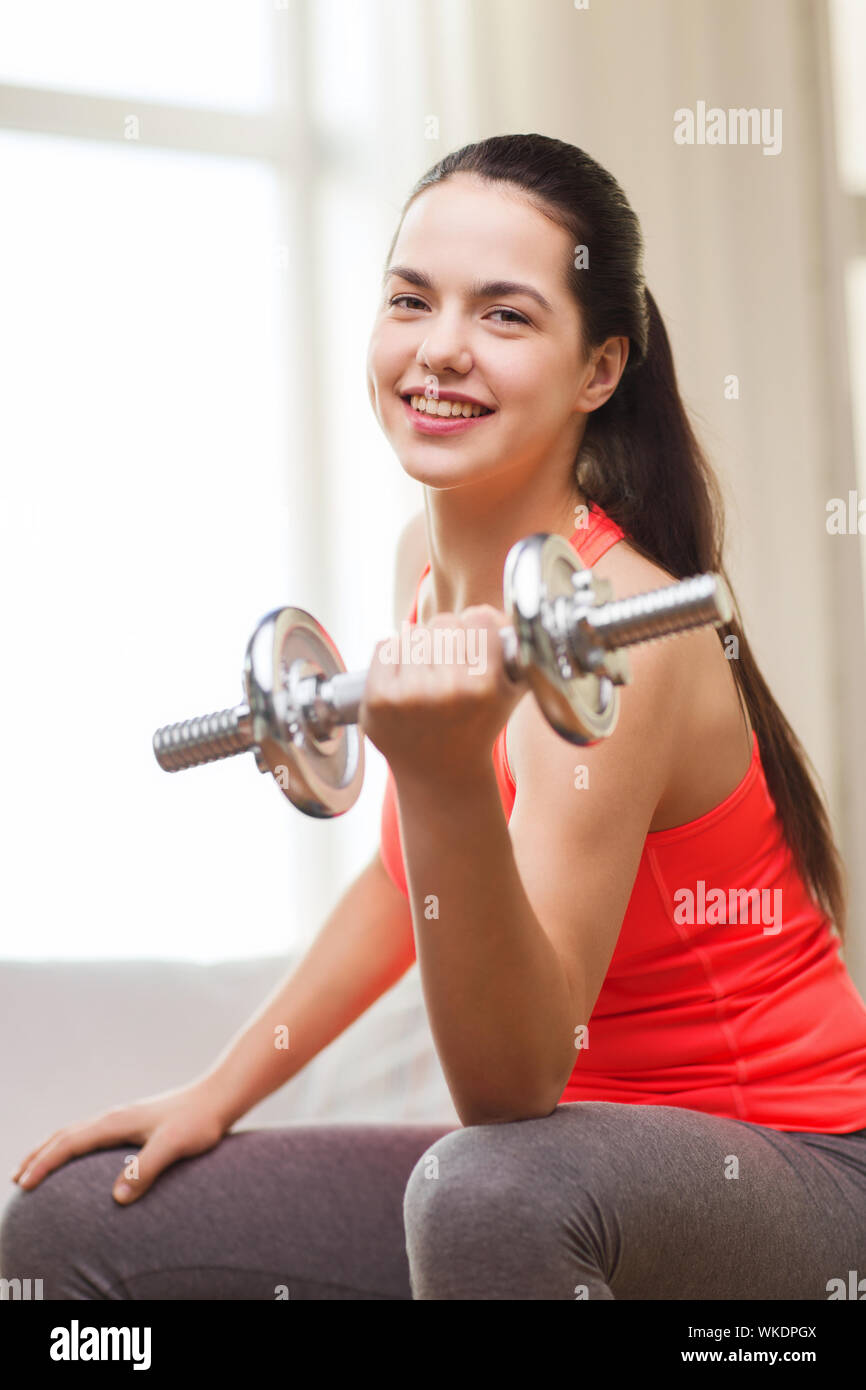 fitness, home and diet concept - smiling girl exercising with heavy dumbbells at home Stock Photo