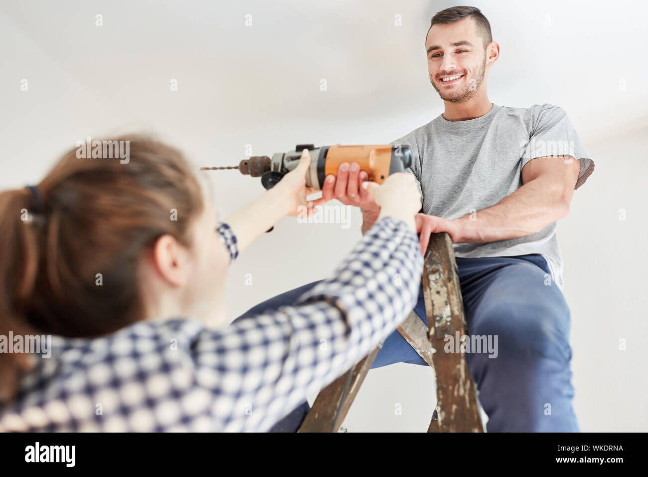 Young couple using drill while renovating apartment or house in teamwork Stock Photo