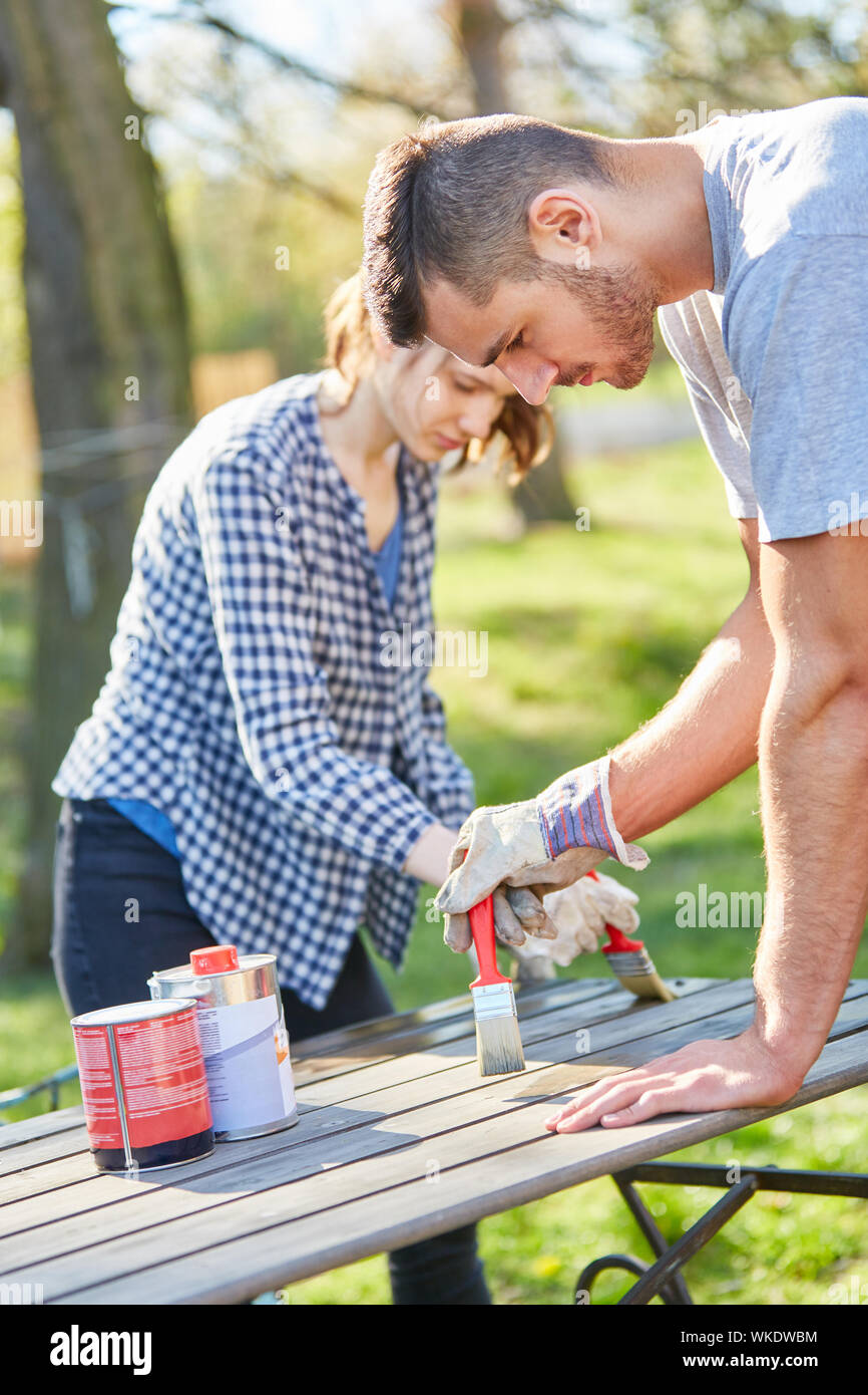 Handyman couple in the garden while painting the furniture with brush and protective paint Stock Photo