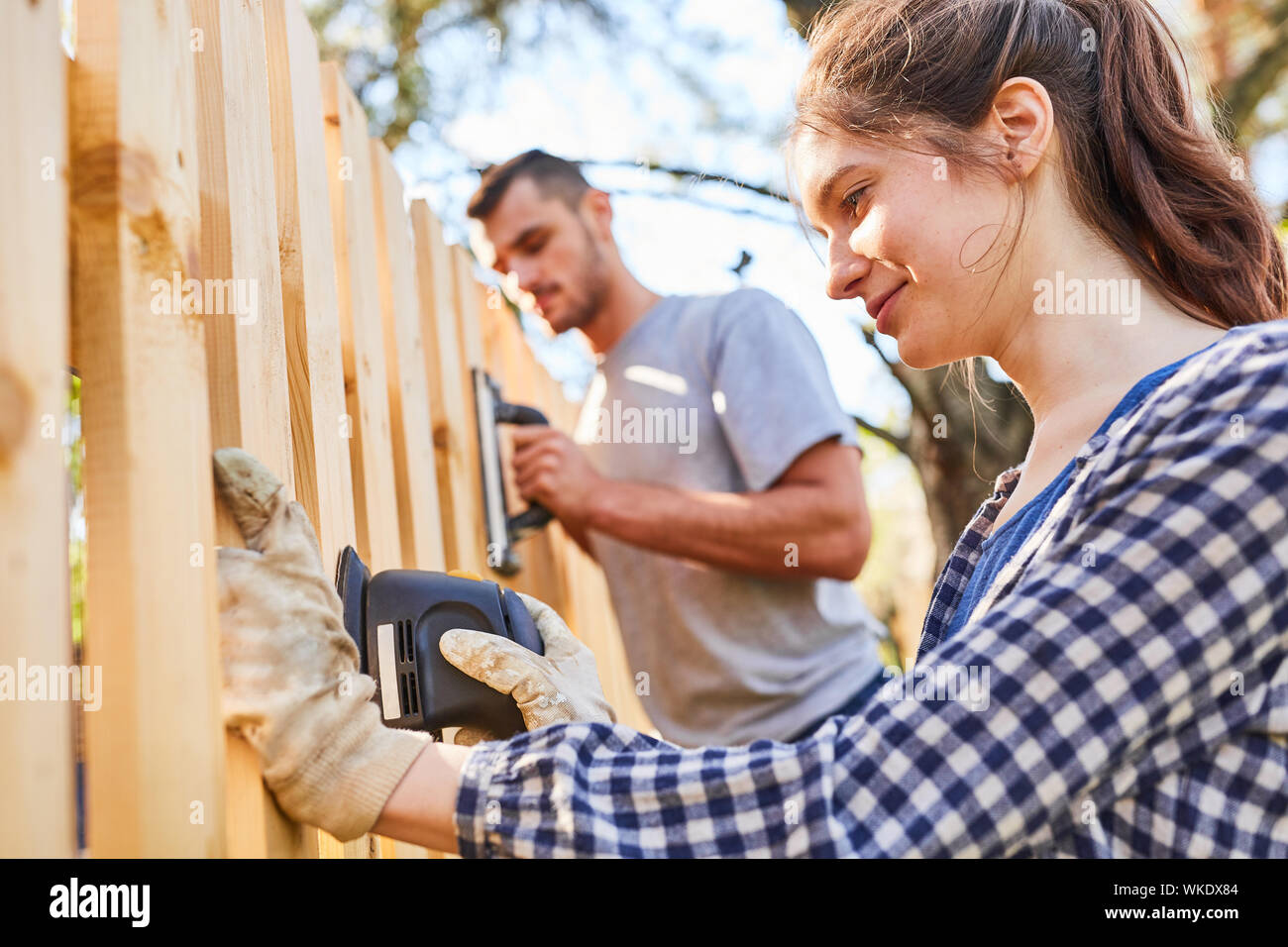 Young couple with grinder grinding at the fence as a handyman work in