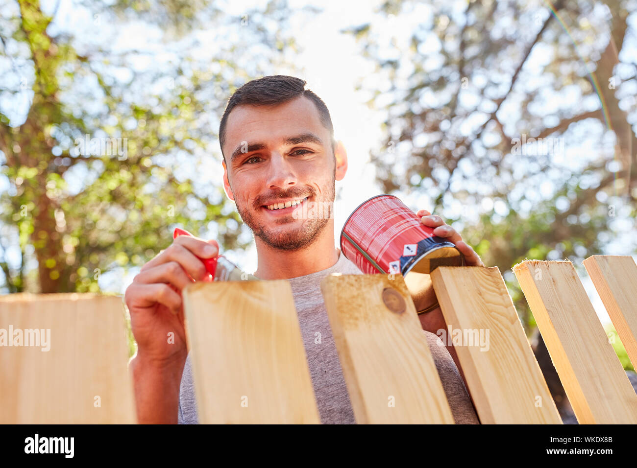 Young man as a handyman in the garden while fence paint or ground with wood color Stock Photo