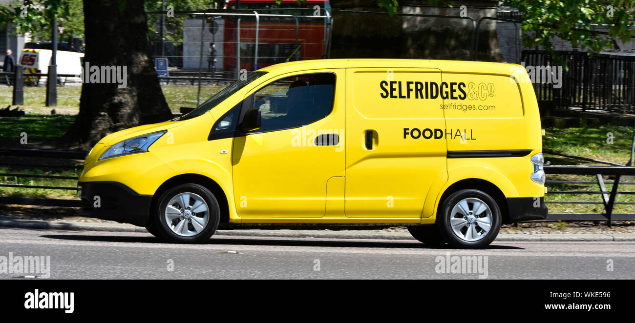 Side view of yellow Selfridges & Co department store delivery van with driver from Food Hall at work driving along Park Lane Mayfair London England UK Stock Photo