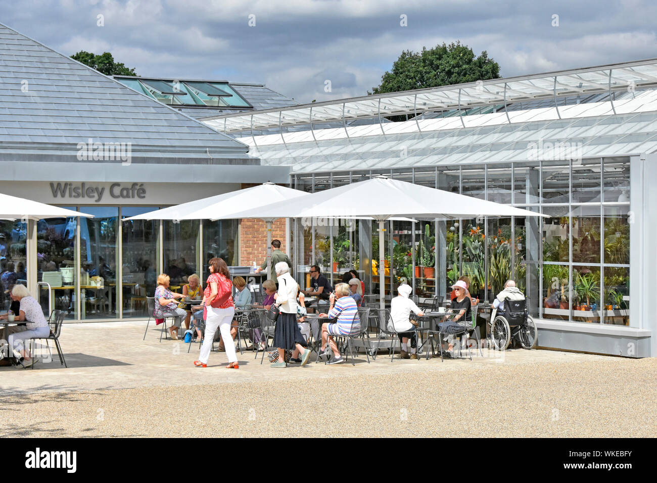 RHS Wisley people at new modern cafe building parasol shade & outdoor tables next to plant shop Royal Horticultural Society Gardens Surrey England UK Stock Photo