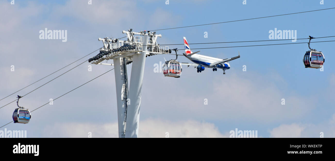 British Airways airplane descending beyond Emirates cable car crossing River Thames at North Greenwich to land nearby London City Airport England UK Stock Photo