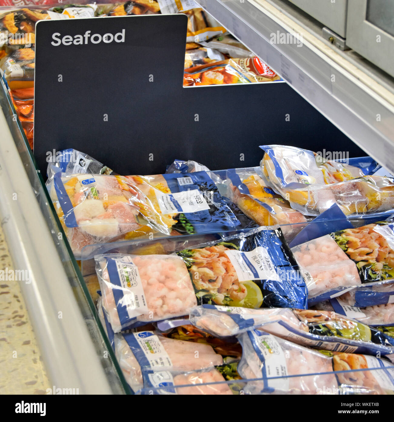 Close up of seafood sign in frozen food supermarket store self service display cabinet with cooked prawns in plastic packaging bags England UK Stock Photo