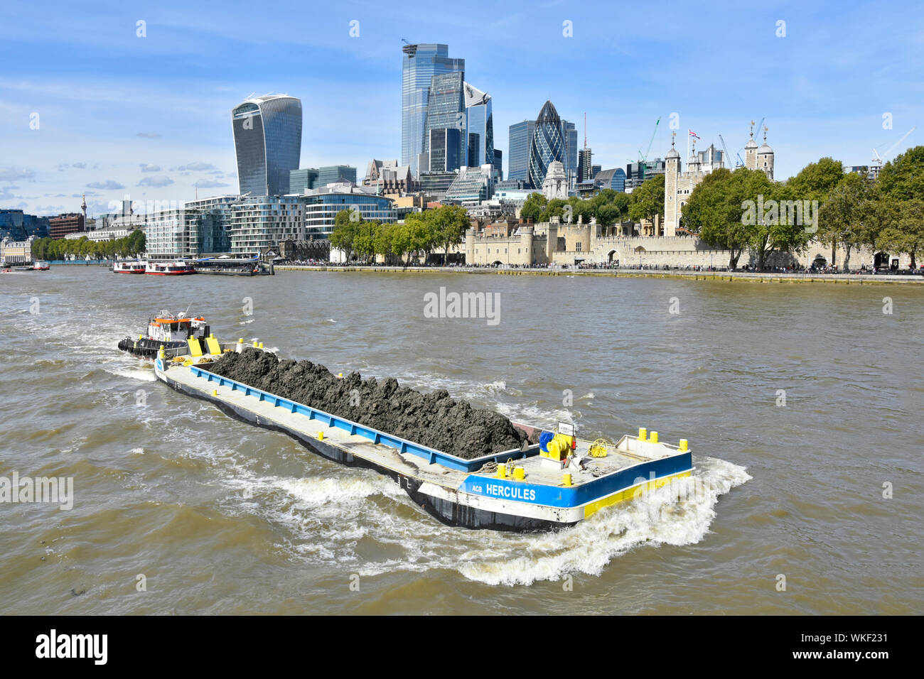 View from above barge & load of soil dug out of River Thames Tideway Tunnel sewer project pushed by tug boat passing City of London skyline England UK Stock Photo