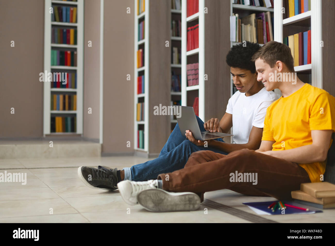 Two teenage guys studying on floor at college library Stock Photo