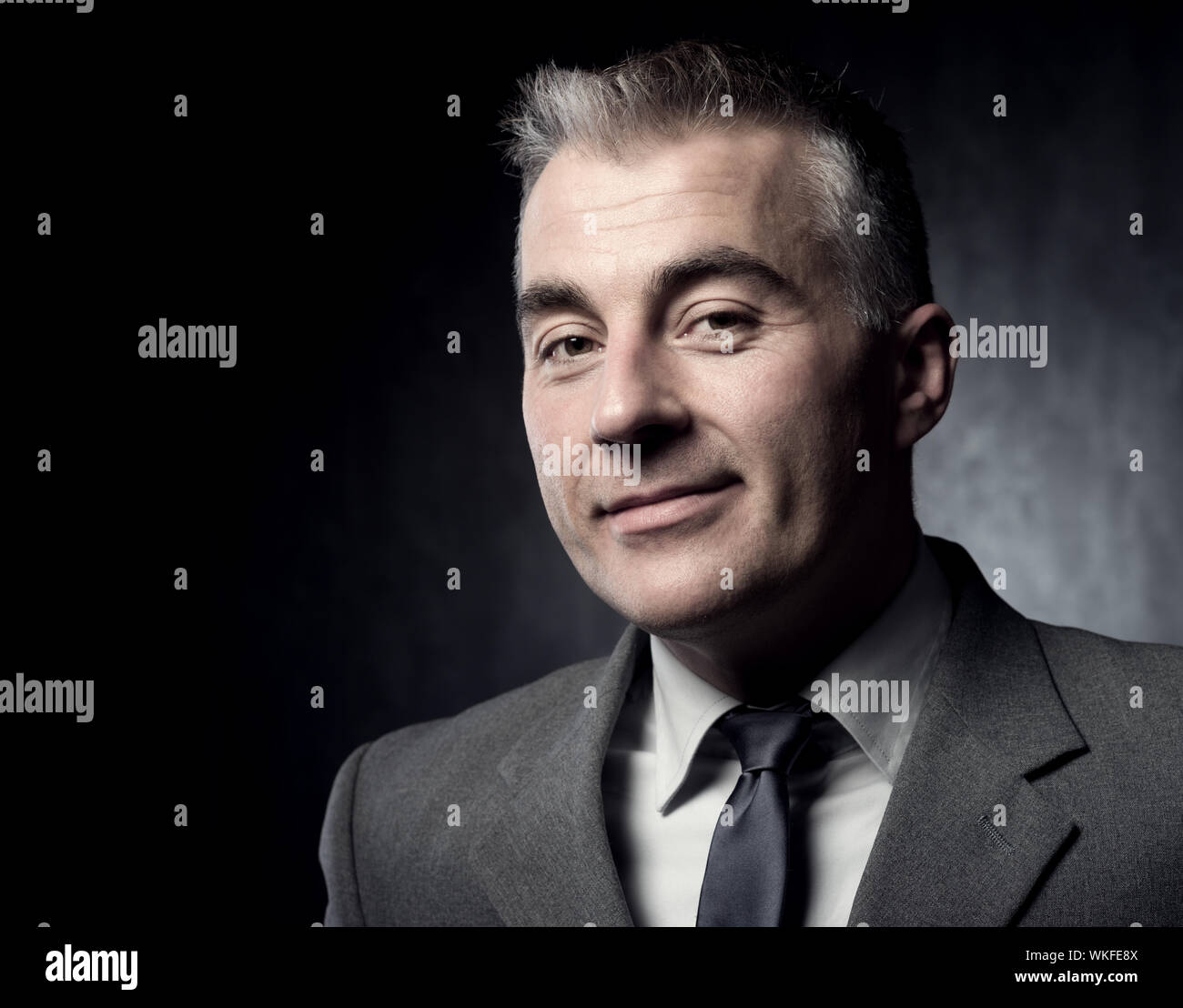 Handsome businessman smiling confidently at camera on dark background Stock Photo