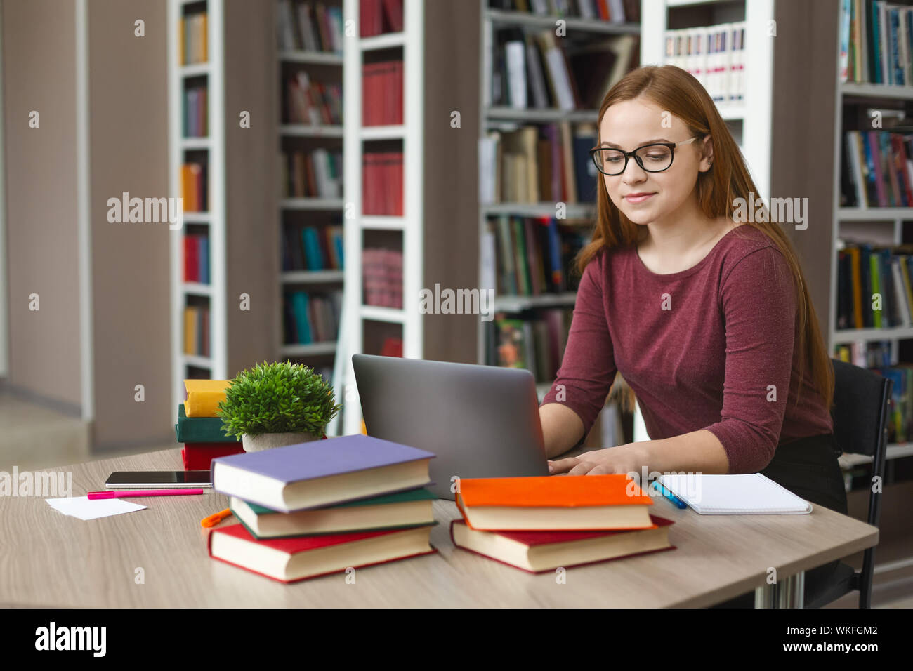 Intelligent redhead girl studying with laptop at library Stock Photo ...