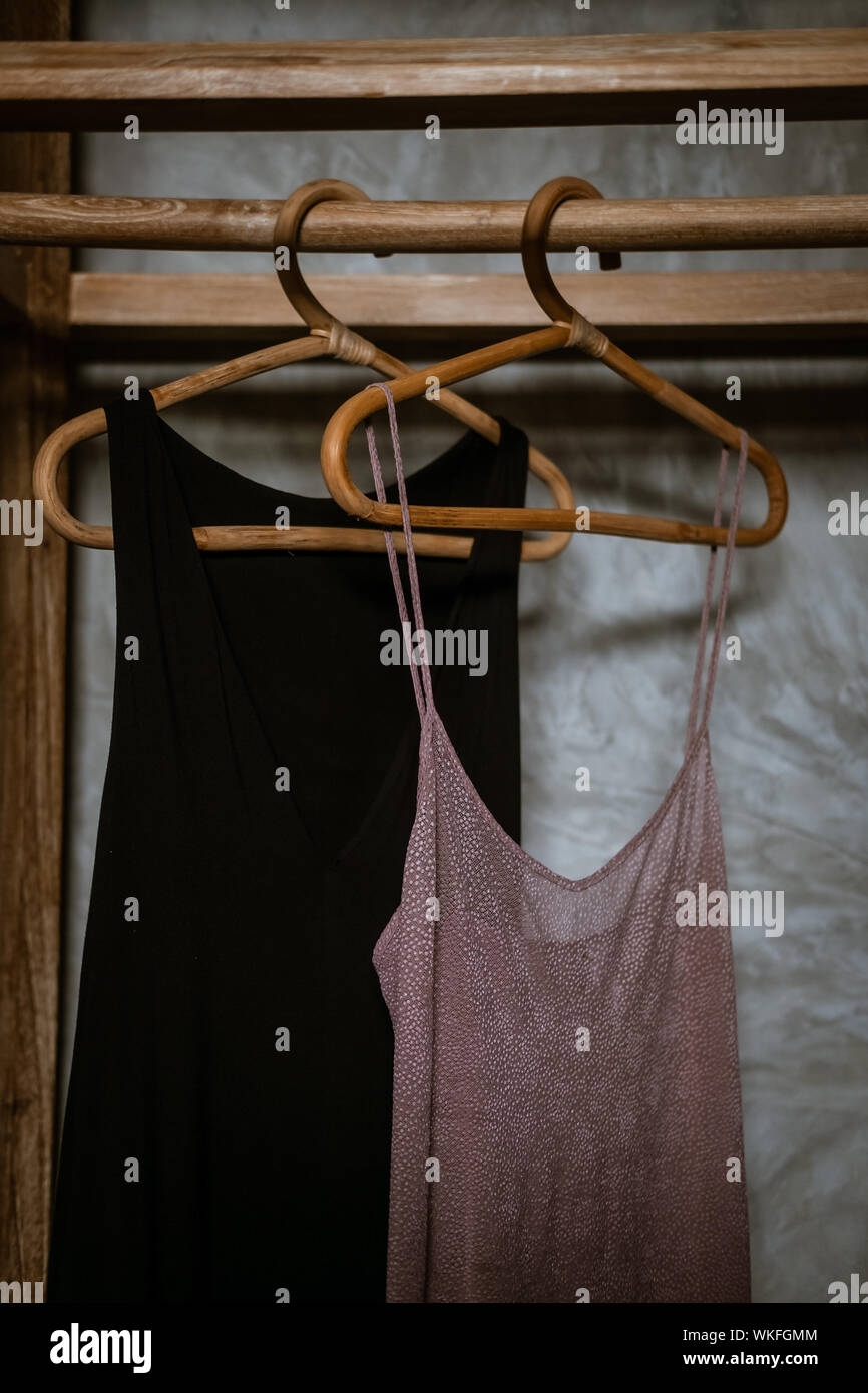 Black and pink nightdresses hanging in boho chic open wardrobe. Clothing rack, rappan wooden hangers. Fashion blogging concept, neutral colors. Loft b Stock Photo