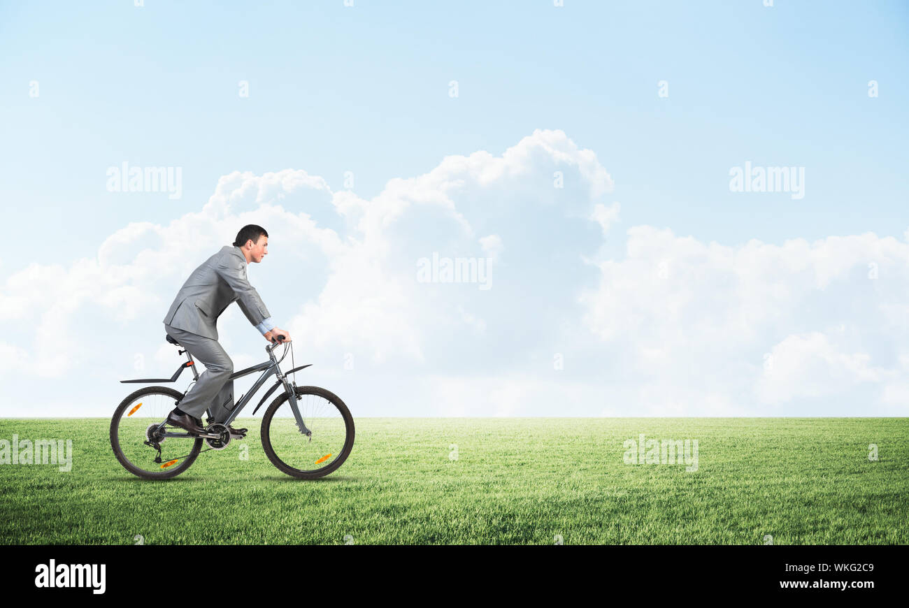 Businessman commuting to work by bike. Man in grey business suit riding  bicycle on green grass. Handsome cyclist on background of blue sky. Nature  lan Stock Photo - Alamy