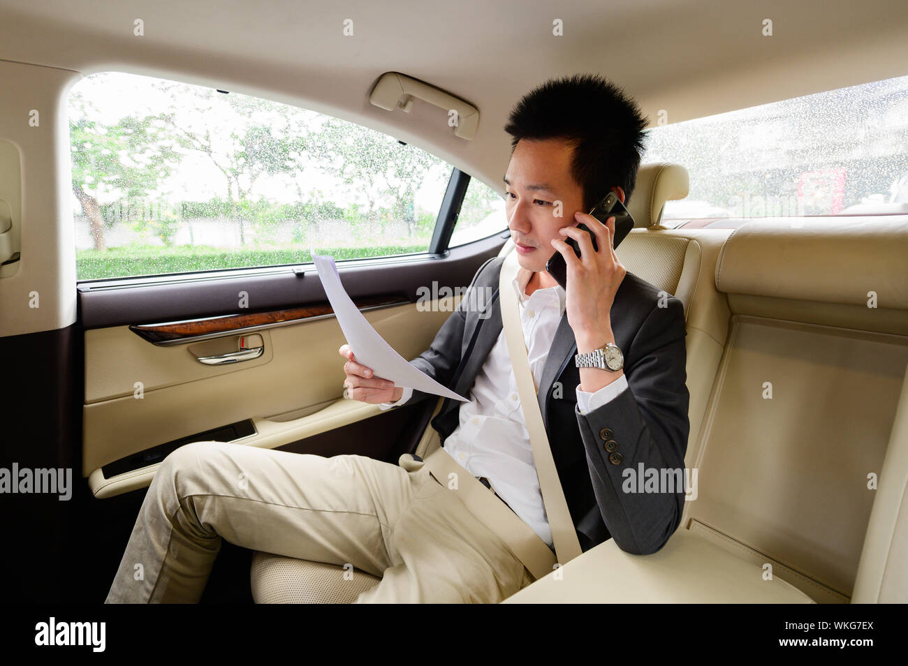 Young man talking on mobile phone and looking through documents while sitting in car Stock Photo