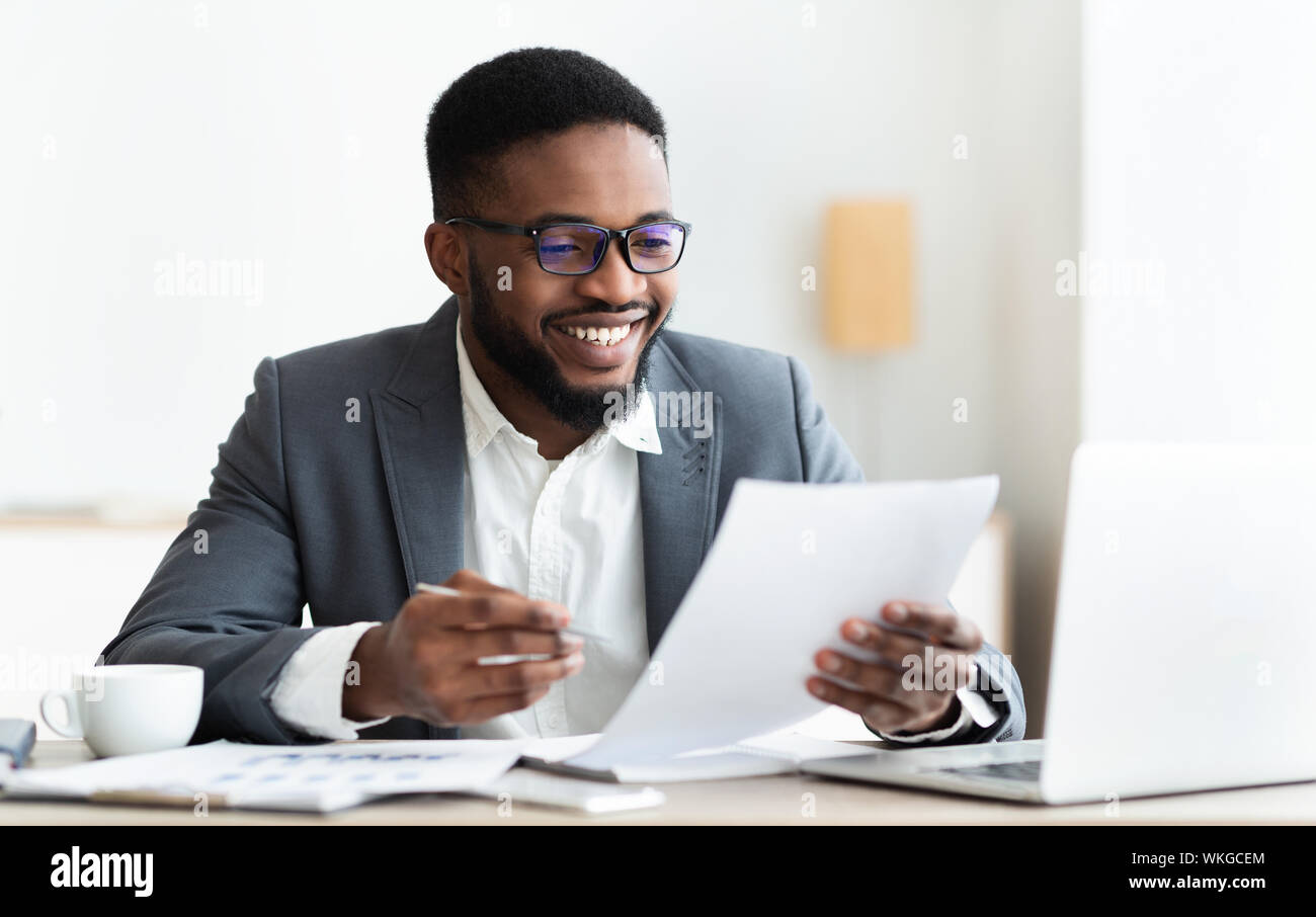 Cheerful black businessman checking reports and making notes Stock Photo
