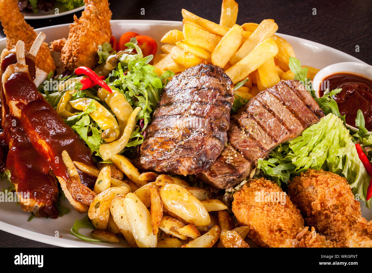 Wholesome platter of mixed meats including grilled steak, crispy crumbed chicken and beef on a bed of fresh leafy green mixed salad served with French Stock Photo